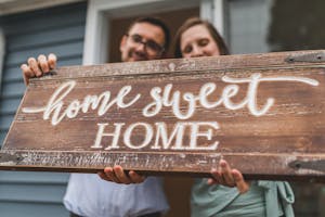 A joyful couple holding a 'home sweet home' sign in front of their new house.